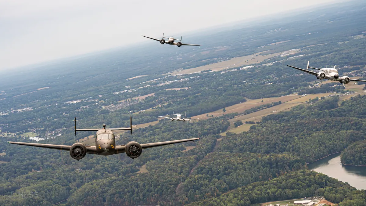 Four Beech 18s spread across a tilted horizon above farmland, with a river winding below